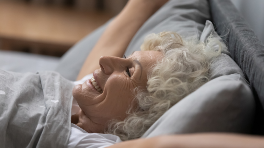 Older lady in bed waking up smiling with arms outstretched