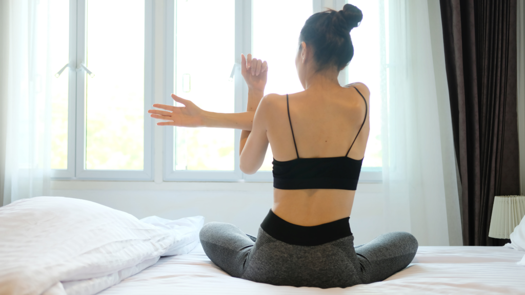 Woman sat on her bed stretching her arms and shoulders.