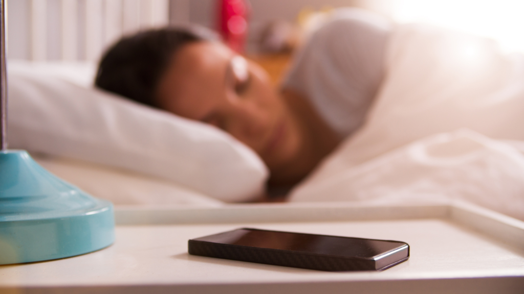 Woman sleeping with phone on bedside table in focus to represent the usage of a sleep app