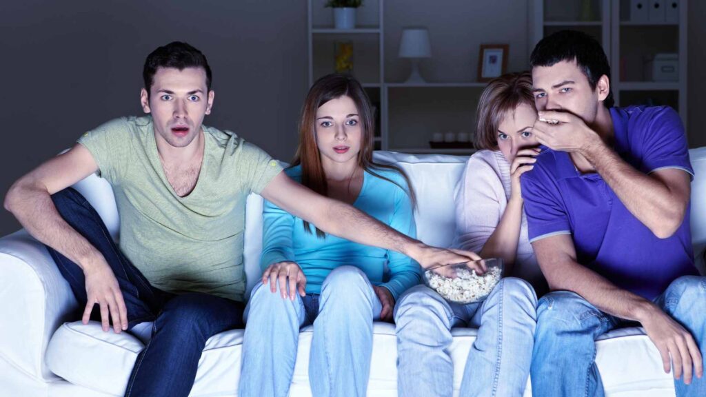 4 adults looking scared sat on sofa watching a scary movie