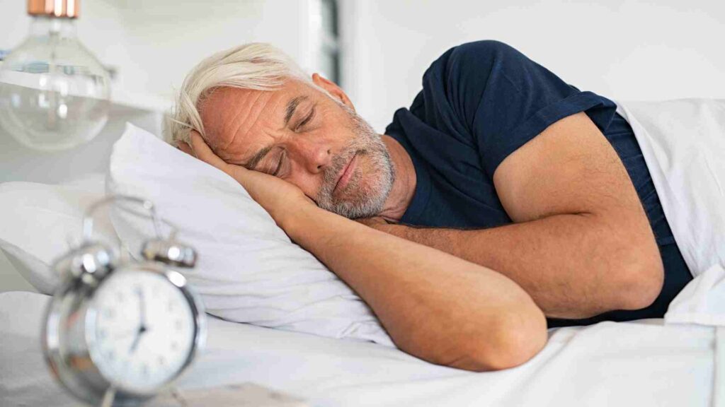 Male asleep in bed with clock next to him