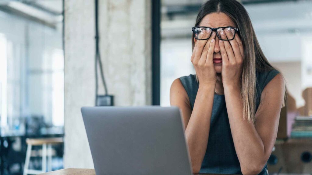 Woman rubbing her eyes at her desk due to sleep deprivation
