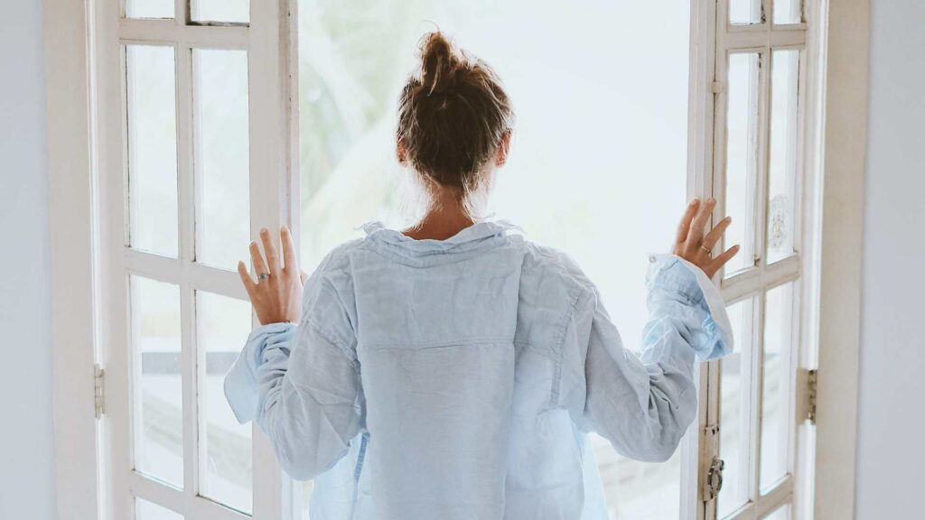 Woman stood at open doors getting bright light exposure as part of best daily morning routine